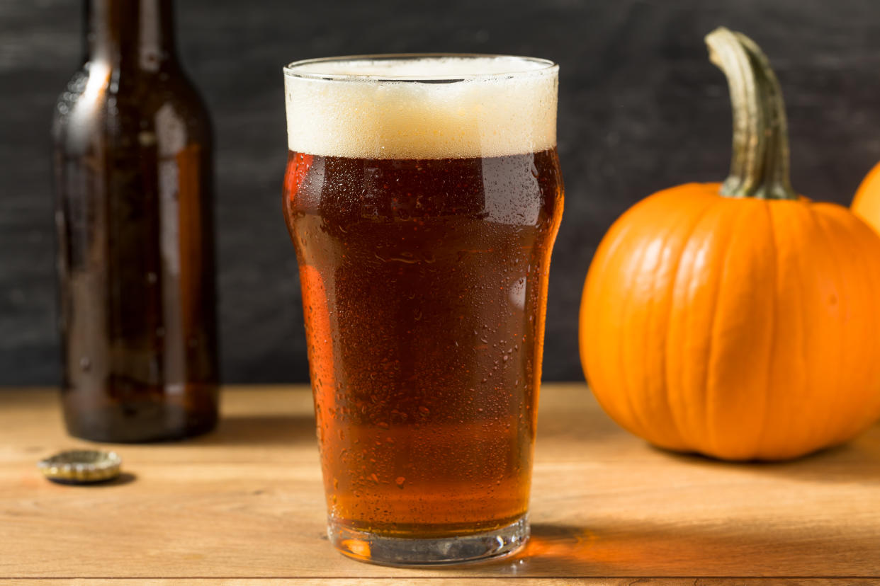 A glass of beer sits on a table next to an open bottle and two small pumpkins.