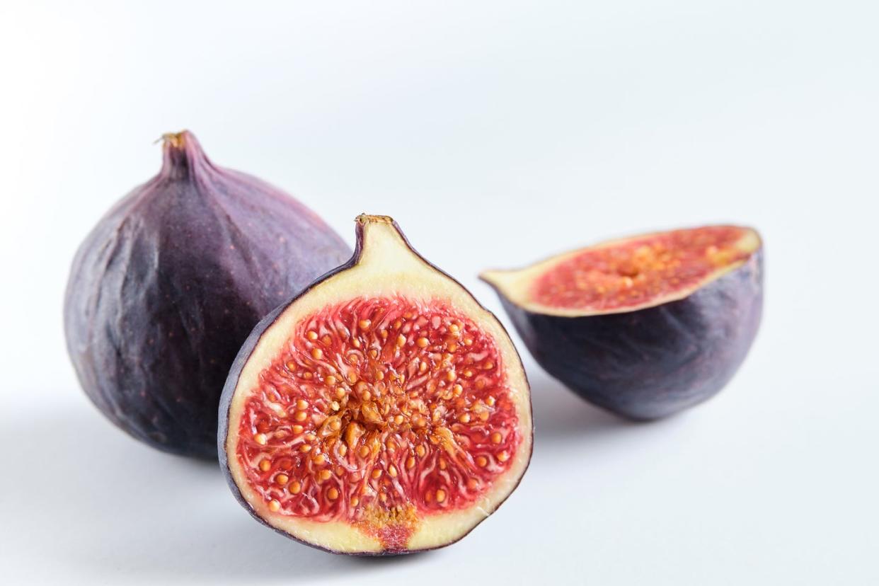 fresh whole and chopped purple figs on a white wooden table food background the concept of vegetarian, vegan and raw food