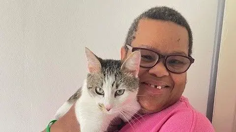 Patsy Wright Patsy Wright with short dark hair and glasses in a pink T-shirt, holding a tabby and white cat. She is smiling at the camera.