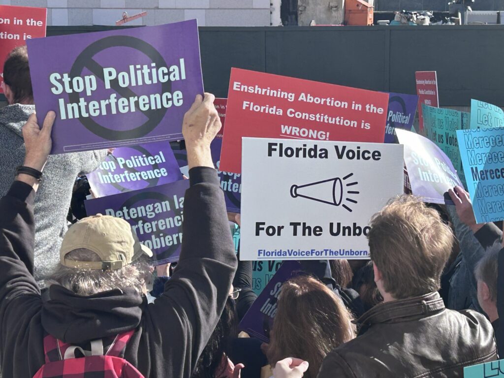 People holding signs saying "Stop Political Interference" and "Florida voice for the unborn"