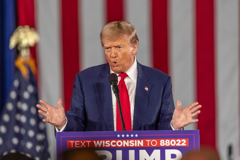 Donald Trump talks into a microphone with his hands out above a sign that says "TEXT WISCONSIN TO 88022"