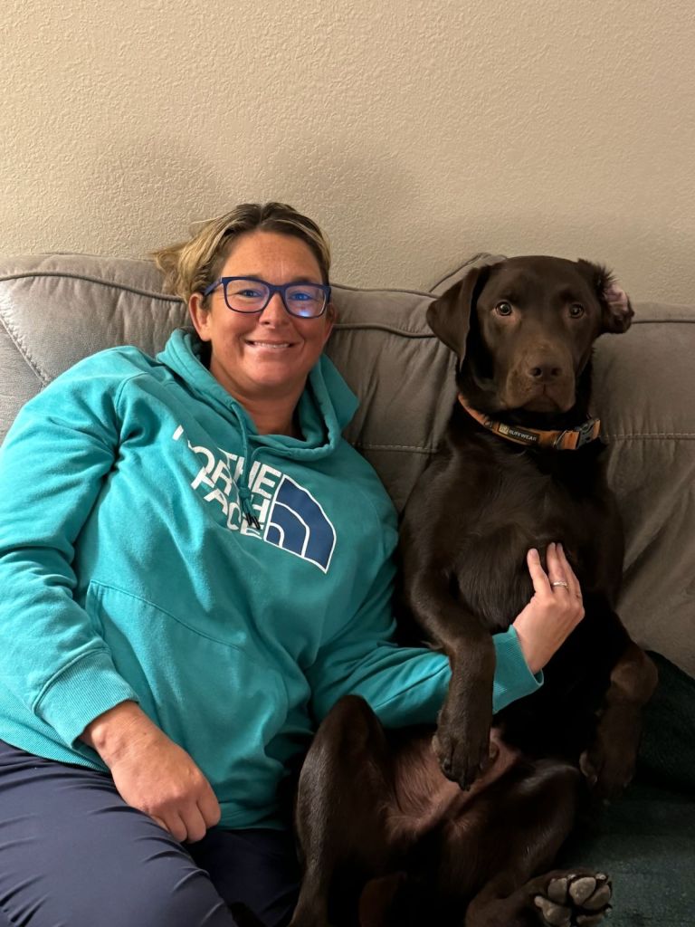A woman sits on a couch with her chocolate lab