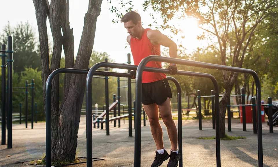 Man working out doing chest dips on parallel bars outside