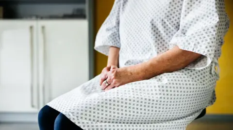 Getty Images A person in a white gown with her hands in her lap. Her face is not visible.