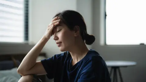 Getty Images A woman with her eyes closed rests her head in her hand