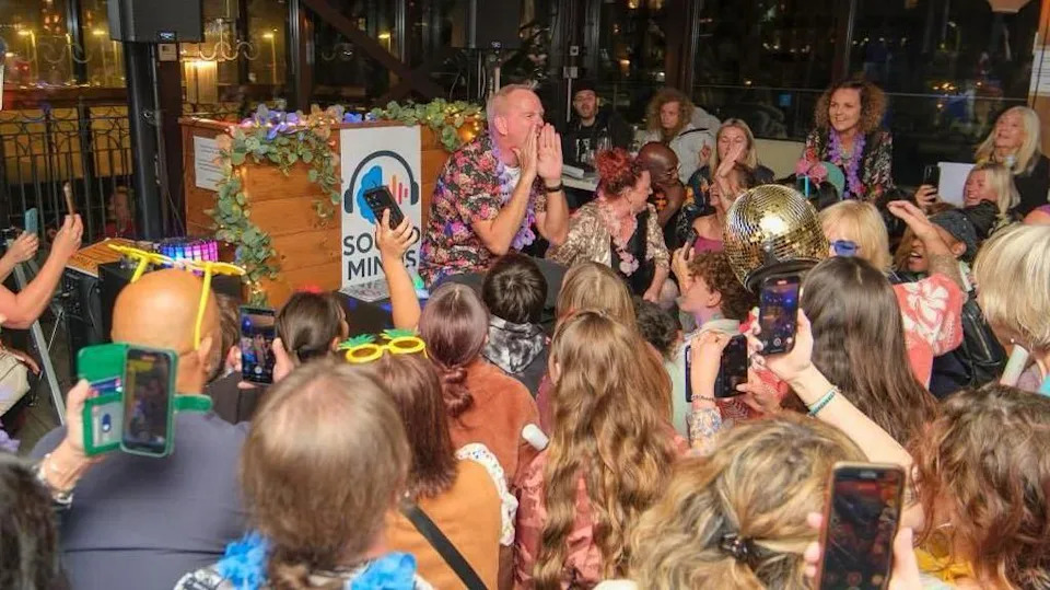 A large crowd of people gather around Norman Cook as he performs at an event.