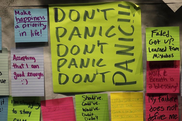 A group of sticky notes in neon colors have writing on them that say 'Don't panic' repeatedly and other notes like 'I am good enough.'