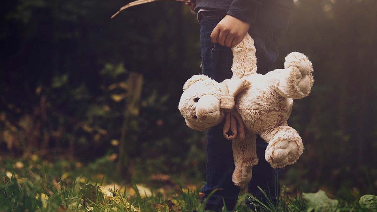 A young boy holding a teddy bear outdoors.