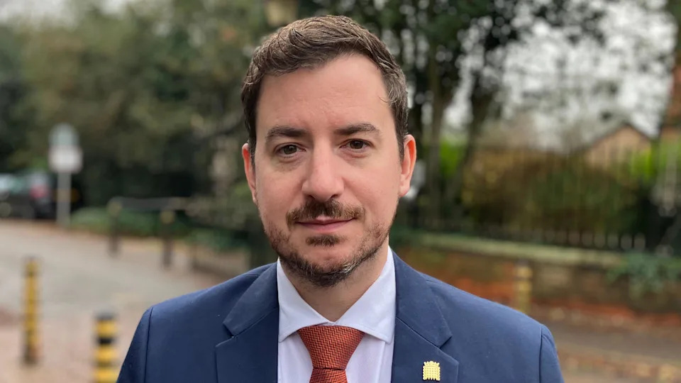 Mike Reader stands outside the hospital. He is wearing a blue suit and orange tie.