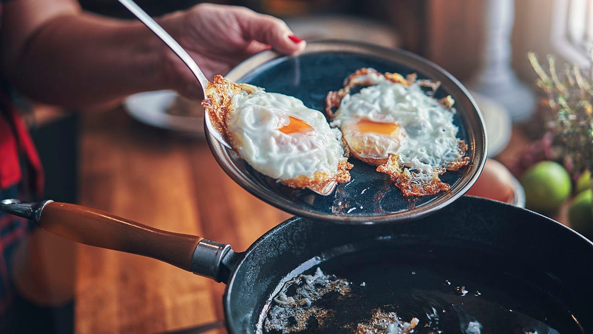 Woman's hands seen putting fried egg on plate from pan.