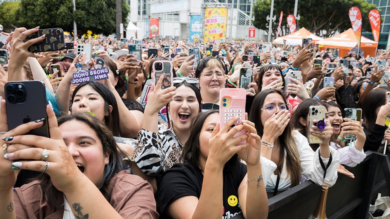 A crowd of fans holding their phones up and cheering outside the Crypto.com Arena for a K-Pop concert in Los Angeles, California.