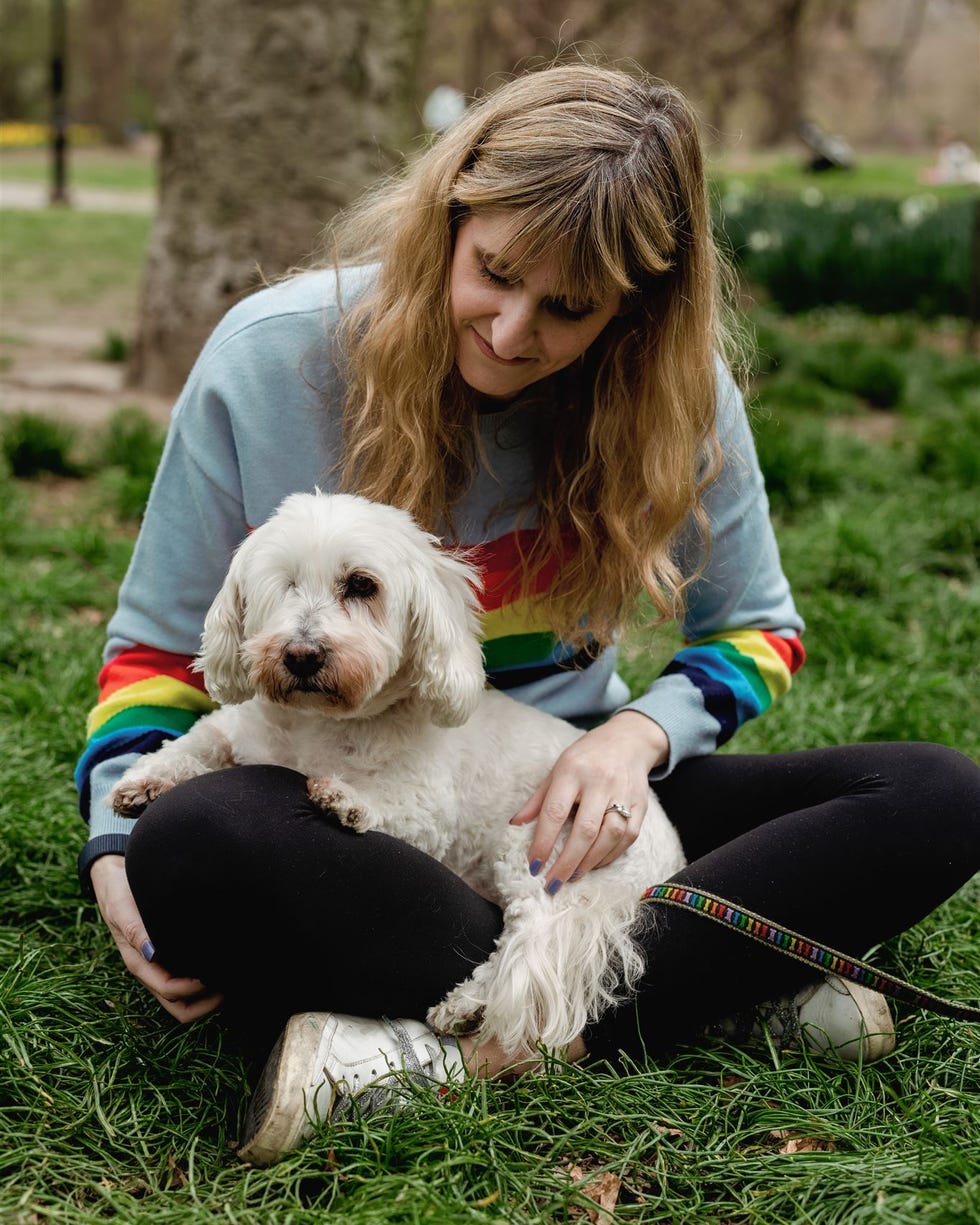 Person sitting on grass with a small white dog.