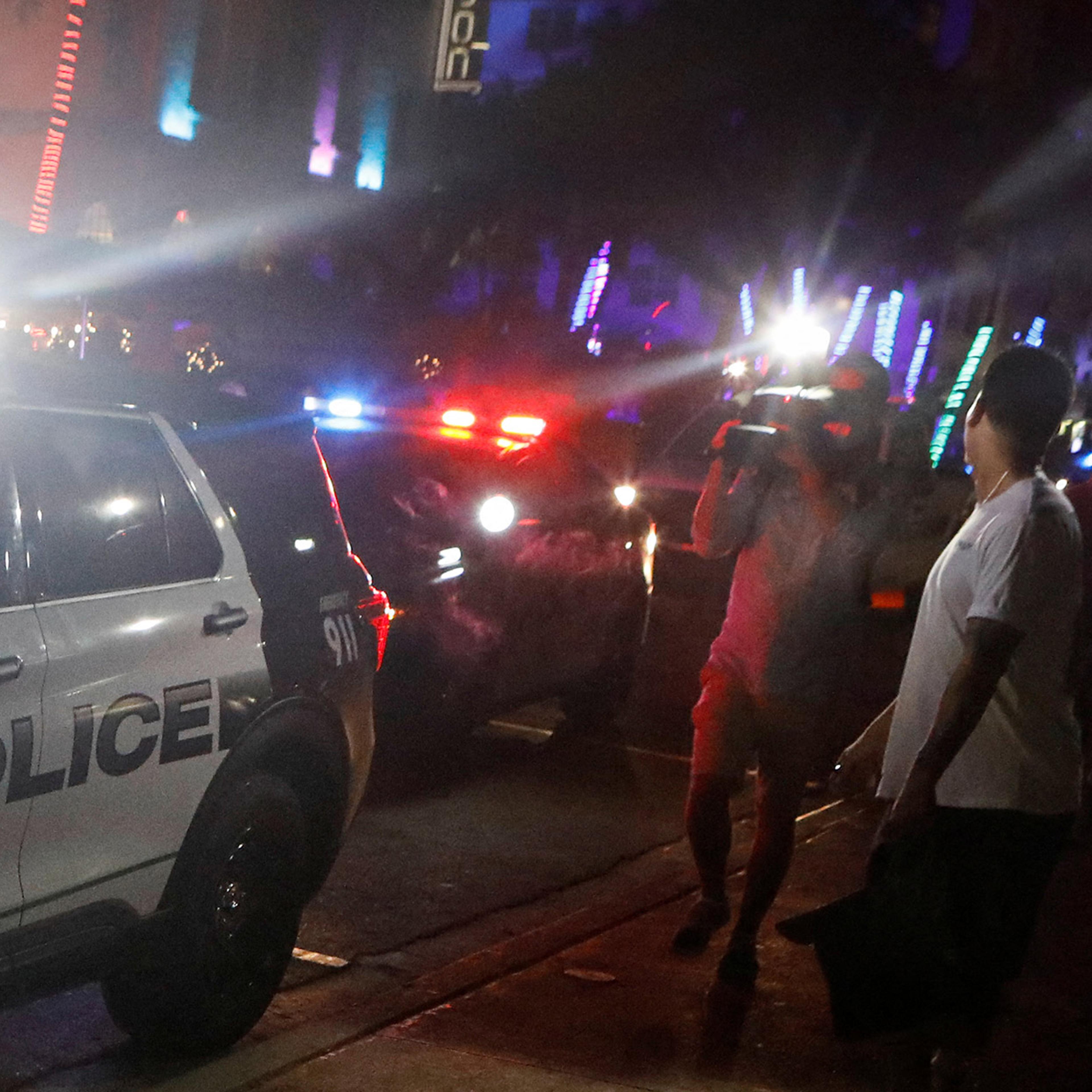 A Miami Beach police car with flashing lights surrounded by people and photographers at night.