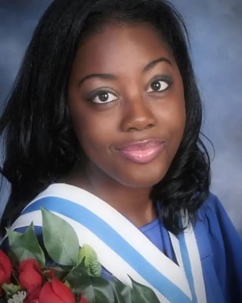 A graduation portrait of a Black girl, wearing a blue gown and holding roses.