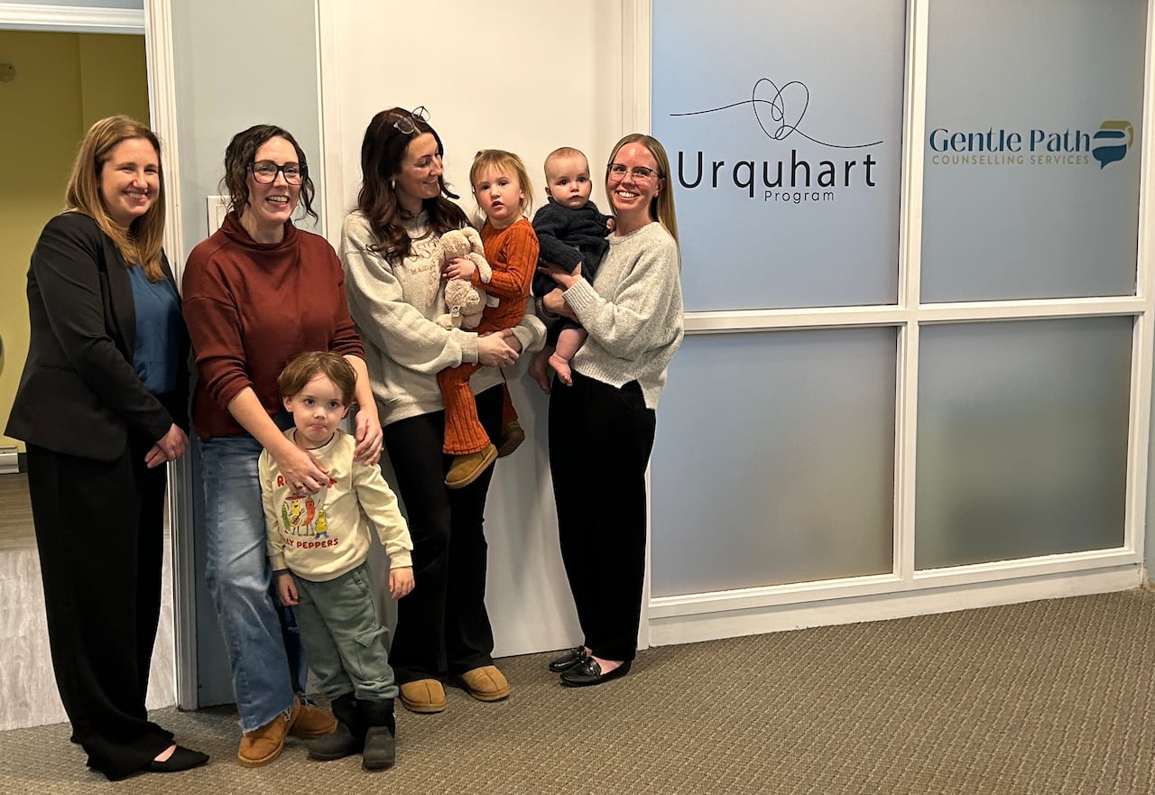 Four women standing, holding kids, in front of a frosted window and door.