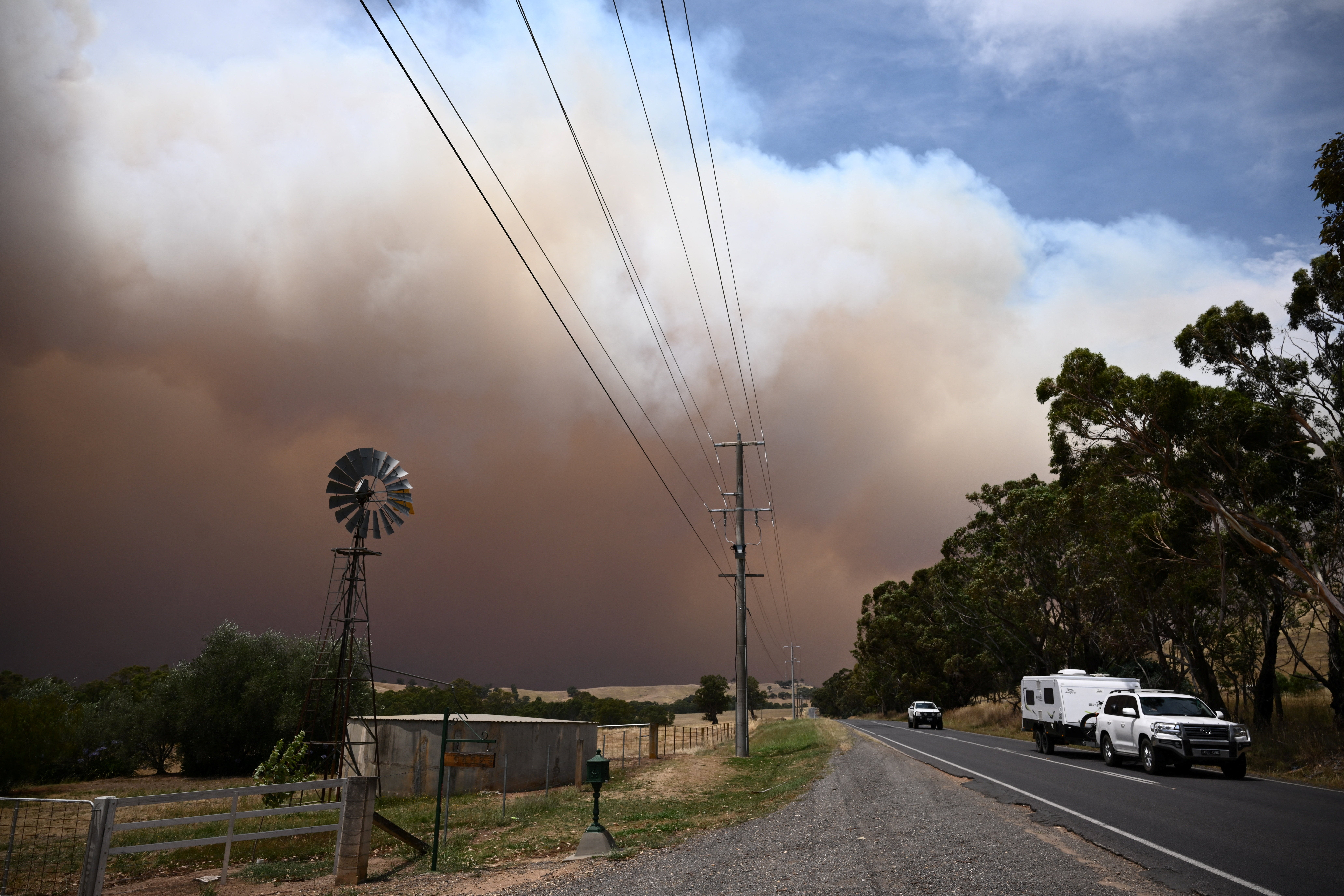 A car towing a caravan drives away from a plume of smoke from the Longwood bushfire, between Seymour and Yea, as out-of-control fires burn in Victoria