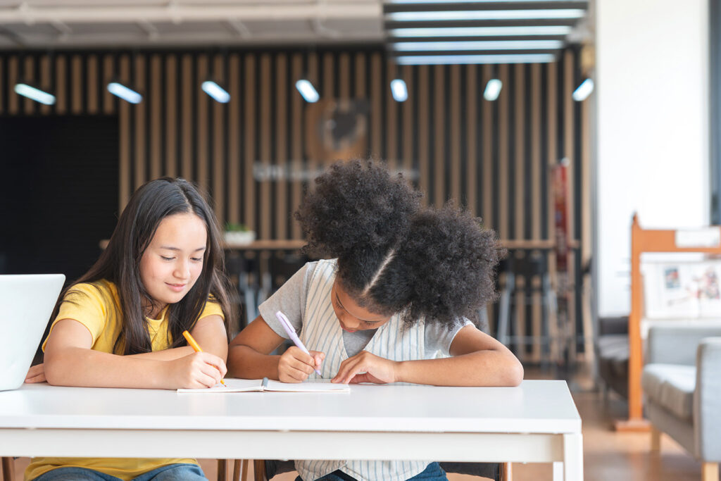 Two female students writing in a notepad together 