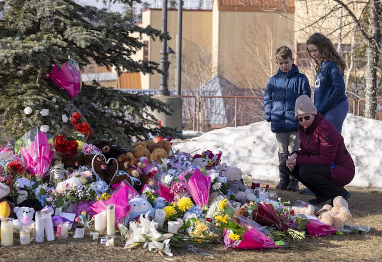 A woman and two children stand next to a memorial made of flowers.