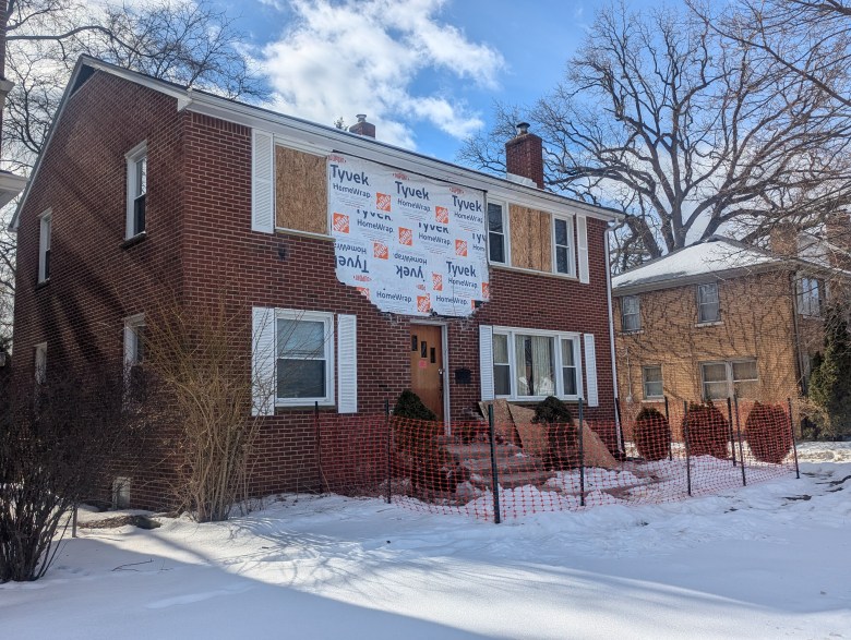 The windows on the second floor are boarded up. Part of the exterior has house wrap. 