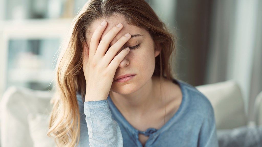 A young woman with a headache pressing her hand to her forehead.