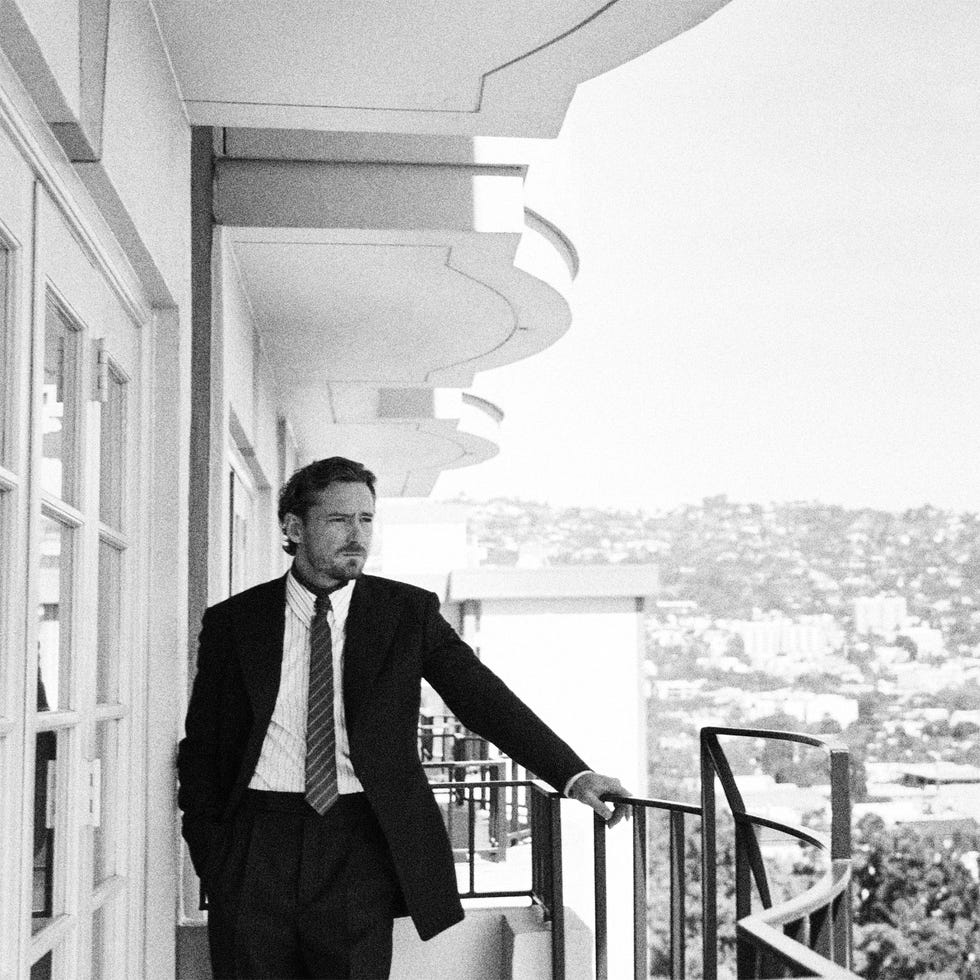 man in suit standing on a balcony overlooking a cityscape