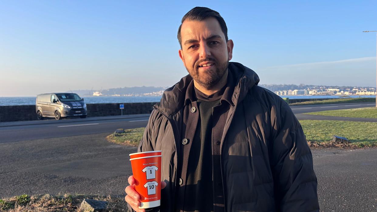 Roll Bar in Guernsey has introduced cups to raise awareness on mental health support. Vijay Wiltshire, owner of Roll Bar holds a red cup with the image of two sports shirts on it.