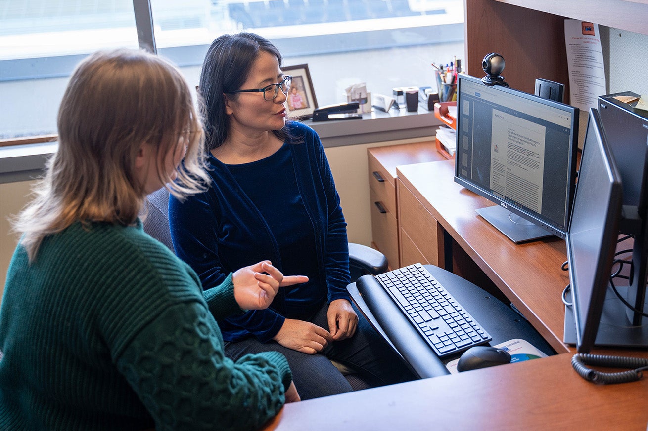 Lucy Zhao looks at a computer screen and talks to a student pointing at it.