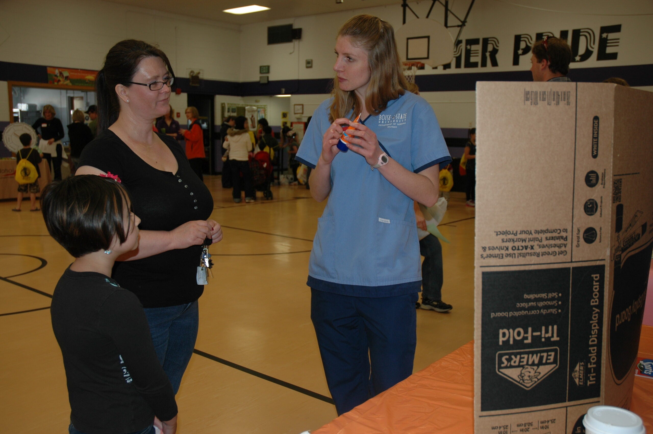 A nursing student shows a mother and child a bottle of sunscreen.