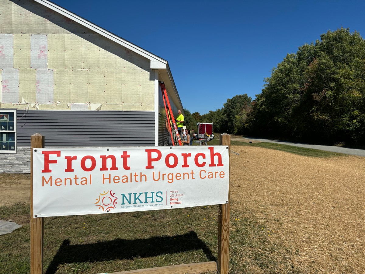 A sign for "Front Porch Mental Health Urgent Care" by NKHS stands in front of a building under construction on a clear, sunny day.