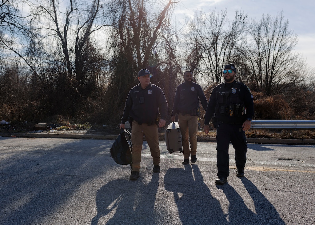 Baltimore Police Officer Angelo Cossentino, Officer Tim Dixon, and Sergeant Rene Aguilera cross the street with the belongings of an unhoused individual who is being transported to a shelter.