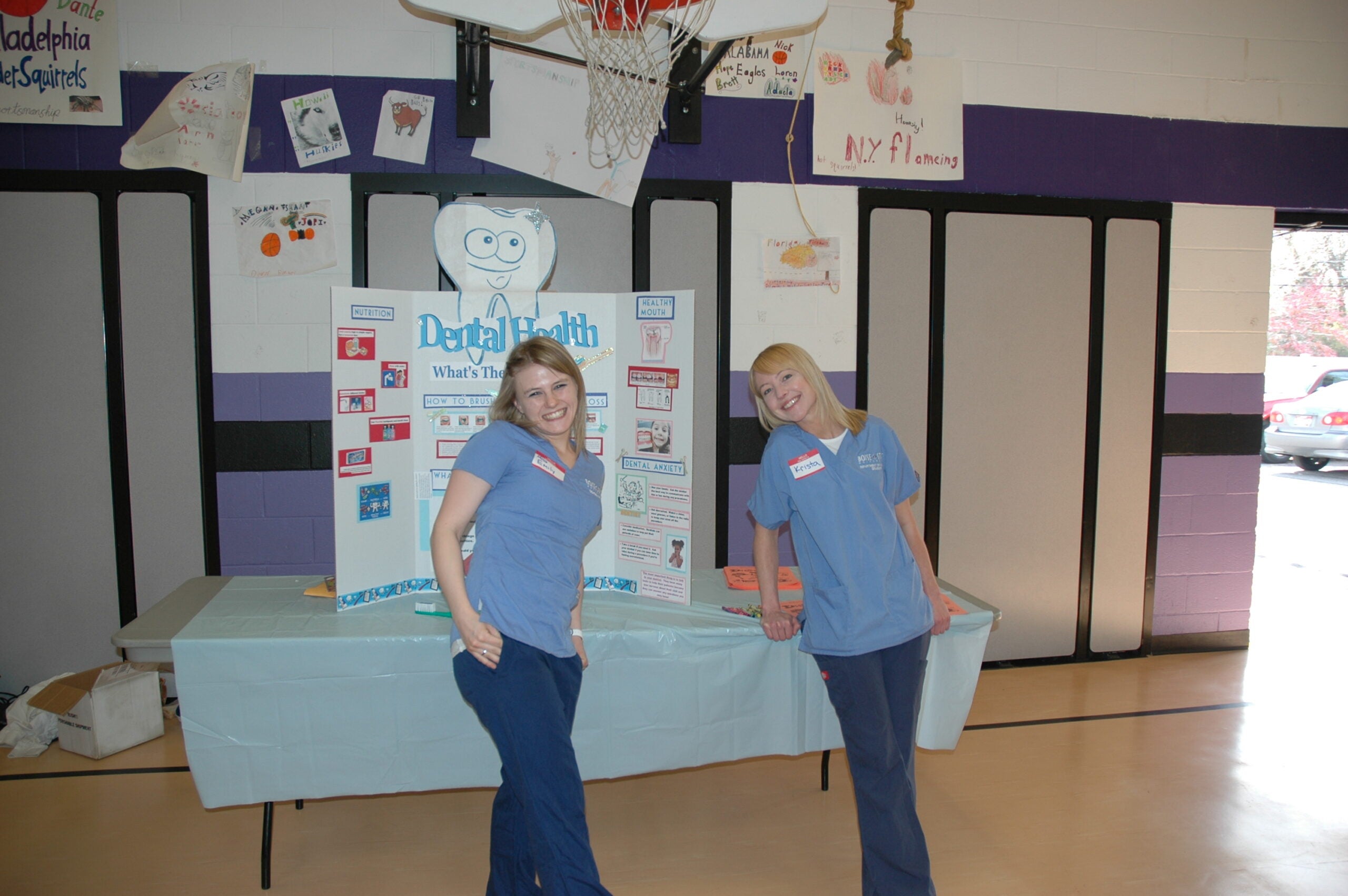 Nursing students pose in front of their table display in a school gym.