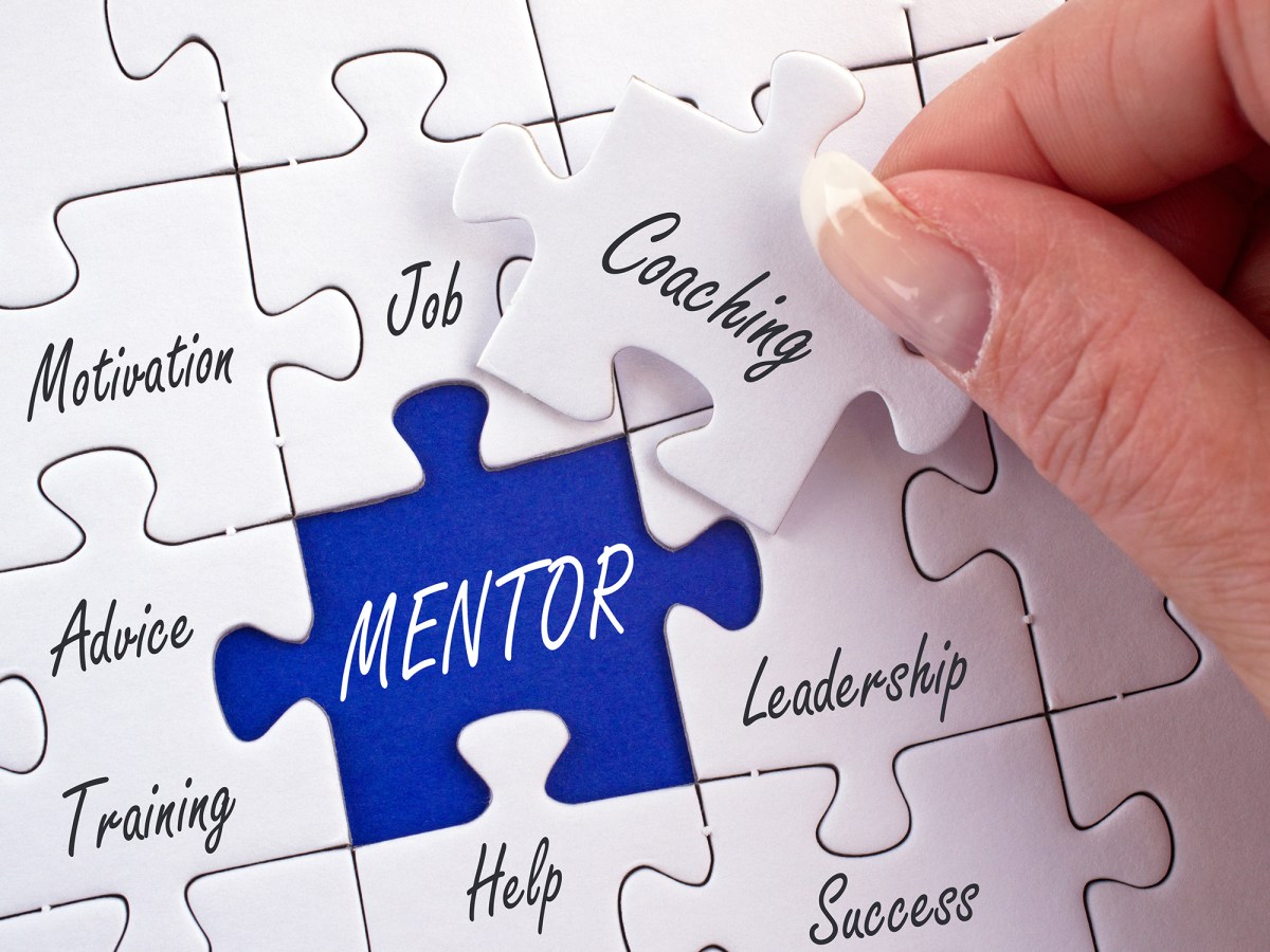 A hand places a puzzle piece labeled "Coaching" into a puzzle, with the word "MENTOR" in the center and other pieces labeled motivation, job, leadership, advice, training, help, and success.