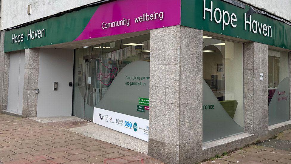 A general view of the Hope Haven hub. The premises are on the ground floor of the corner of a building. The front has large shop windows, partially frosted. The signs in green and pink.