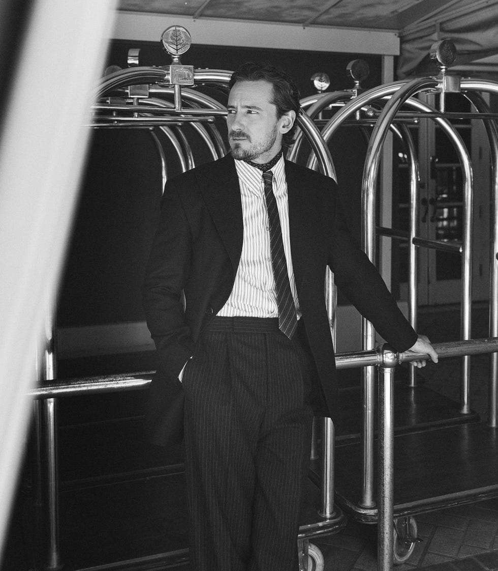 individual in a tailored suit poses near hotel luggage trolleys