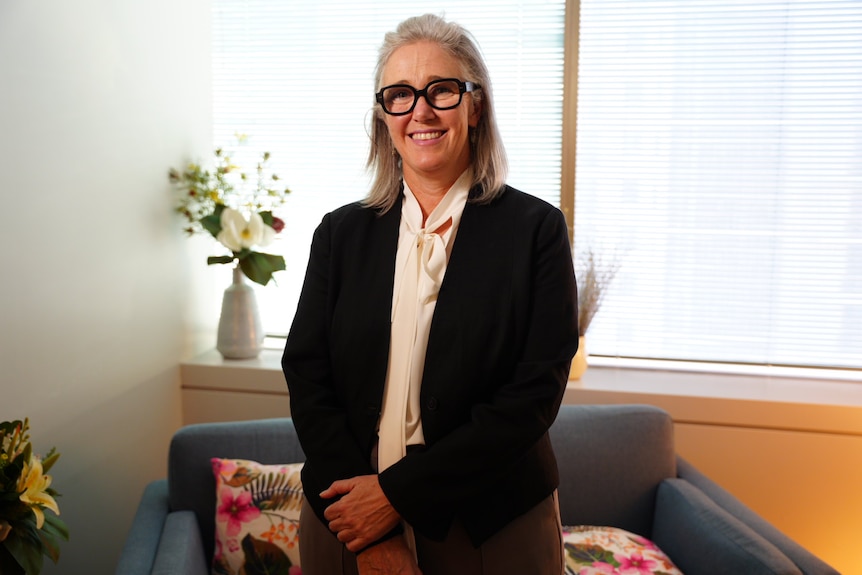 Dr Sarah Dominguez stands indoors in front of a vase with flowers smiling at he camera