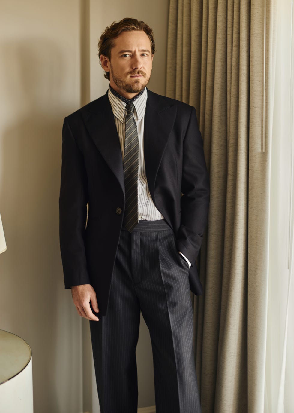 a person dressed in formal attire stands beside a curtain