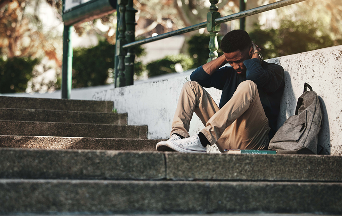 Young man with head bowed and sitting against a staircase.