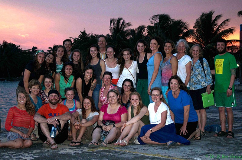 Group photo of 29 people on a beach at sunset.