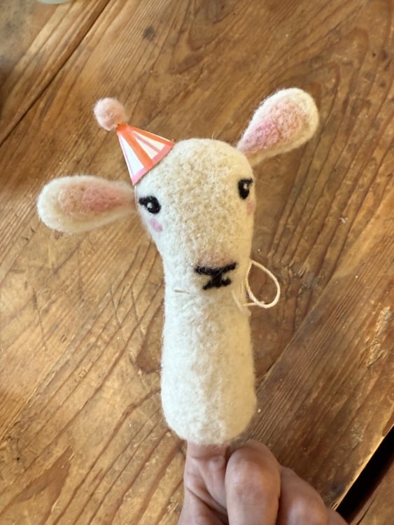 A white lamb finger puppet, wearing a tiny orange and pink party hat.