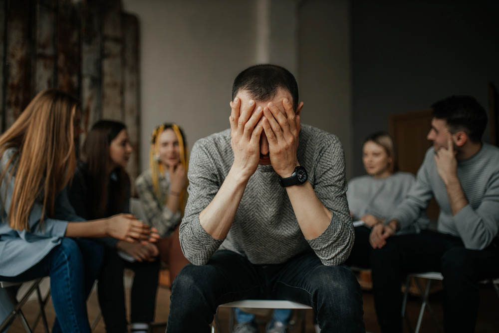 young caucasian man tired of drinking alcohol or drugs, members of anonymous alcoholics club gathered to share experience of getting rid of problem. guy close face with hands. help, support concept