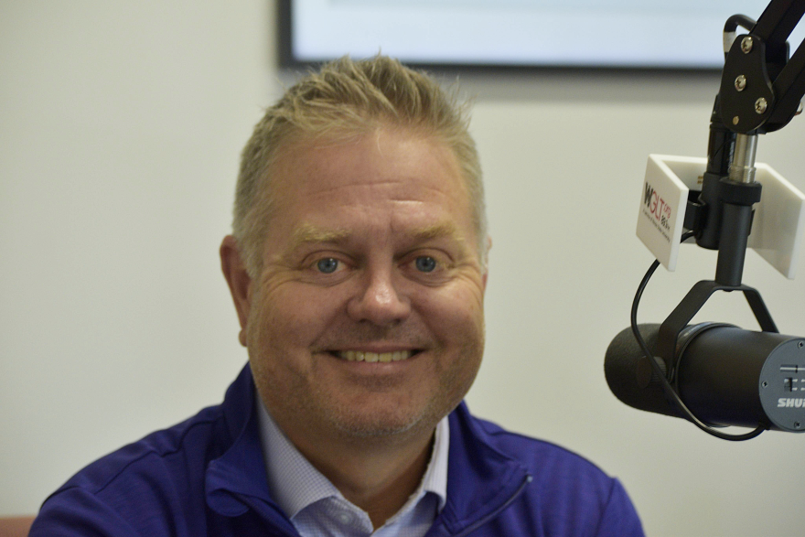 Man in blue smiles behind microphone.