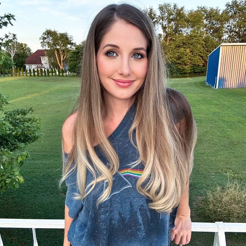Christina Buttons looking at the camera from an outdoor balcony, with her backyard and a blue shed in the background.