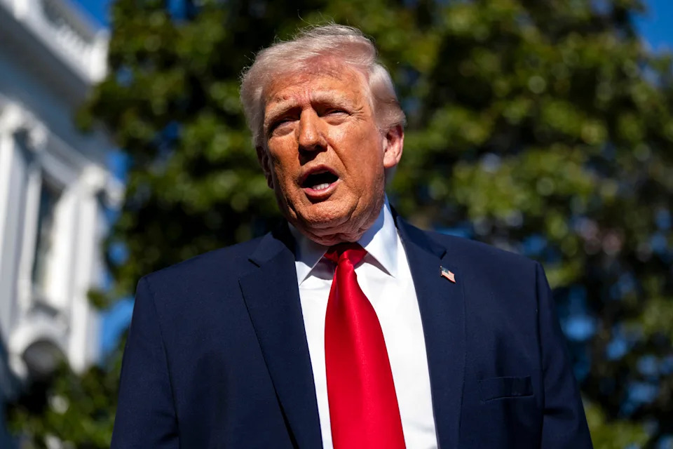 Man in a suit speaking outdoors with trees in the background