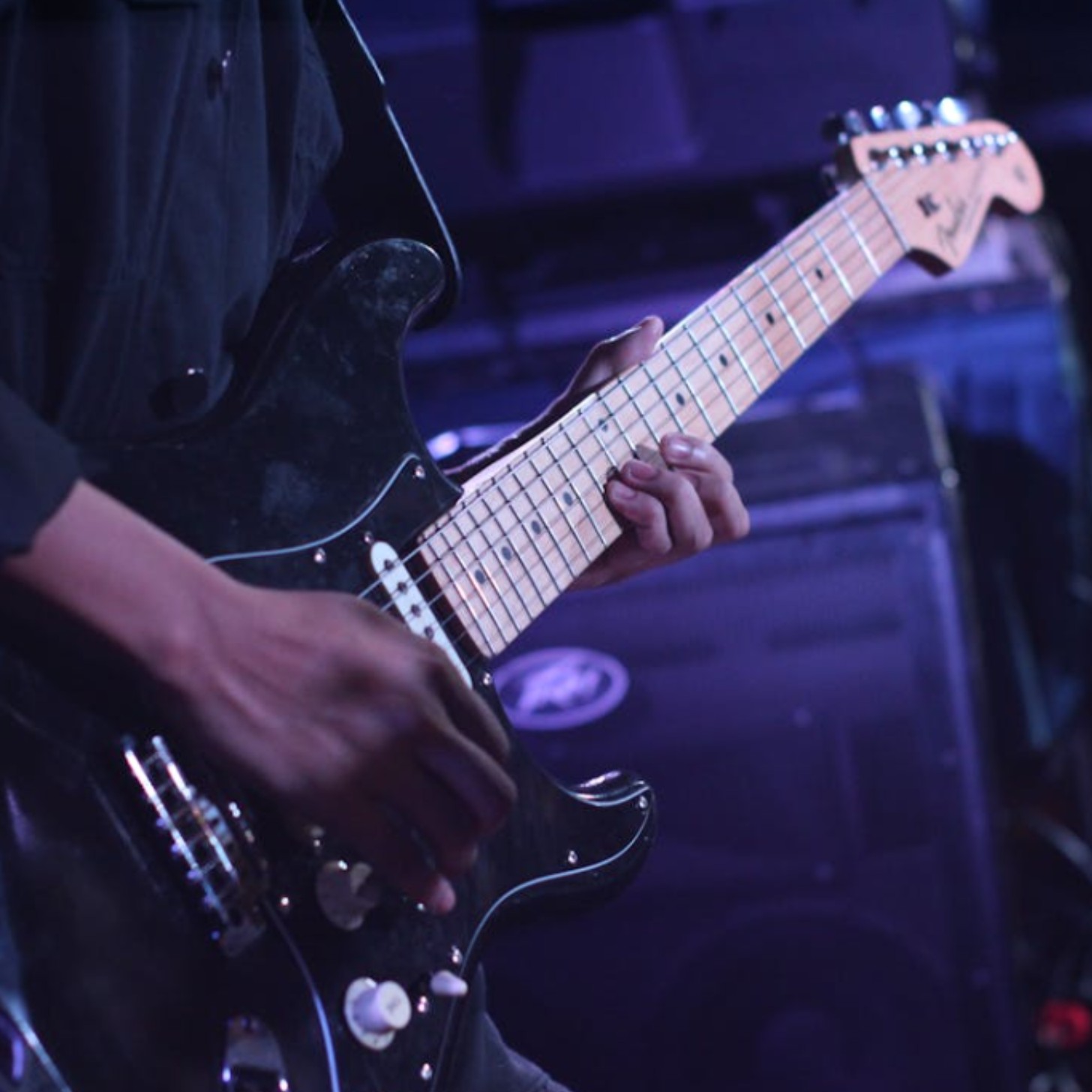A man plays the electric guitar on stage in a close-up picture that only includes his midsection and hands.