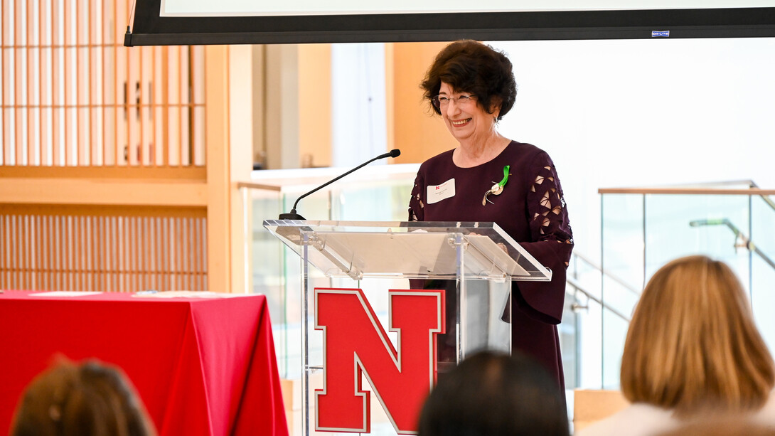 A white woman with a dark brown bob stands at a podium smiling in a dark maroon dress.