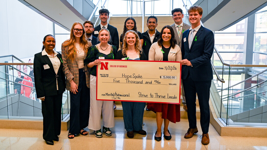 A crowd of people gather around a large check, written to HopeSpoke, for five thousand dollars.