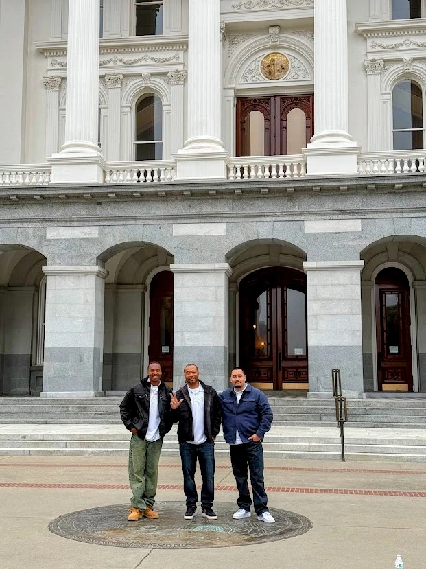 Three men pose in front of a stately building.