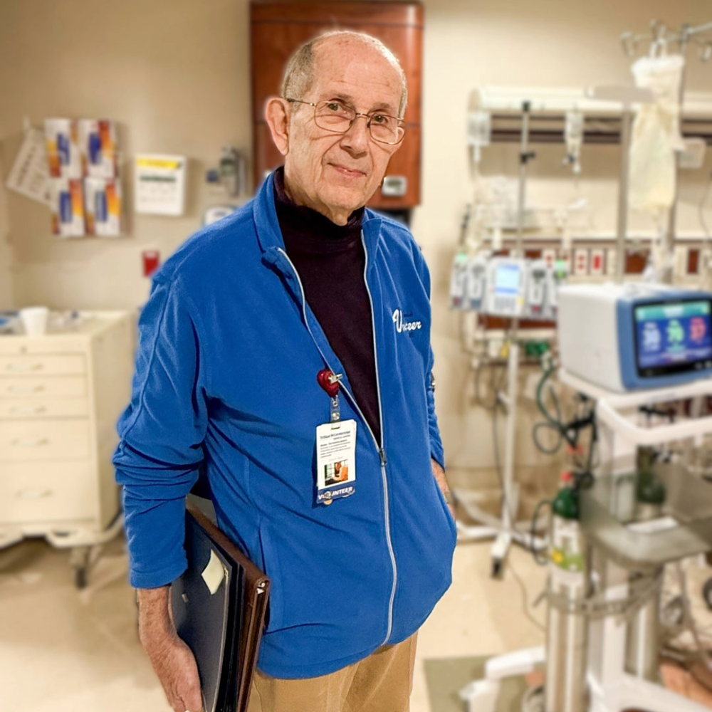 Jim Leath stands in hospital room wearing a blue jacket and holding a portfolio