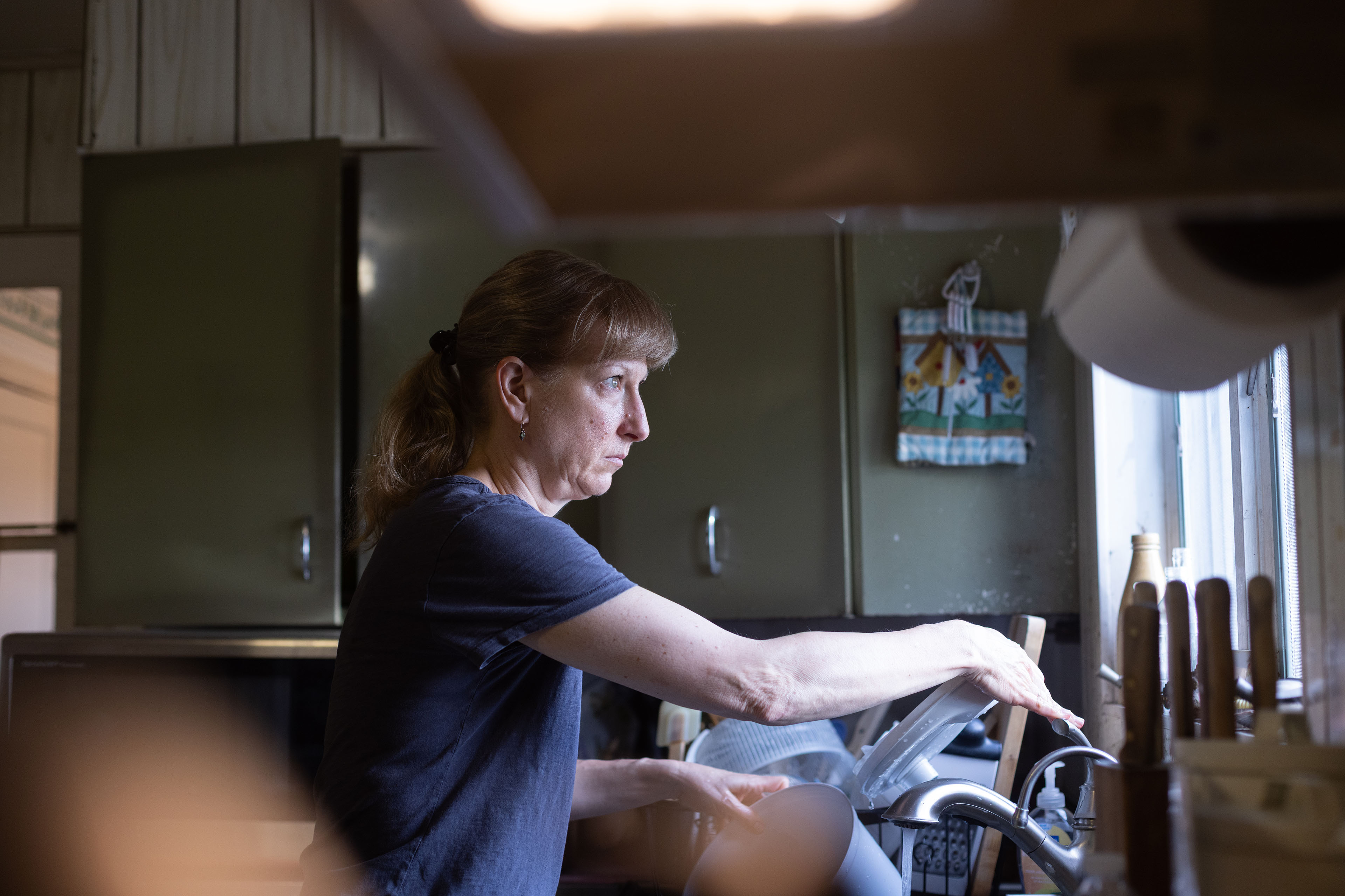 A woman stands at a sink while looking out a kitchen window