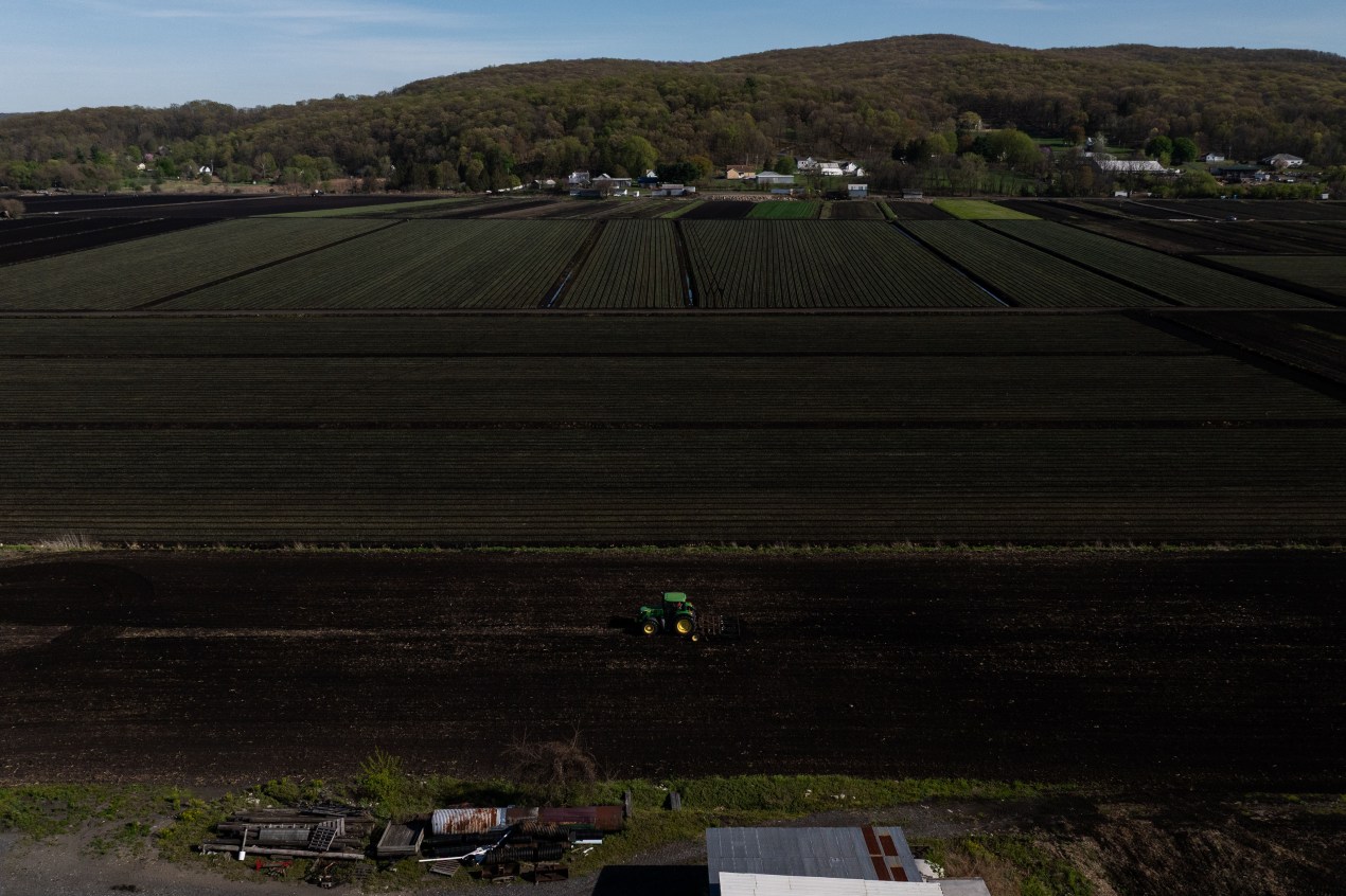 A drone photograph of farm fields with hills in the background and a green tractor in the foreground